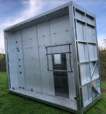 A full-scale test structure featuring steel cladding panels and a central window designed for real-world environmental testing.