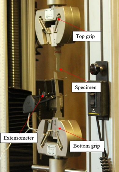 An Instron material testing machine with a mounted specimen, extensometer, top grip, and bottom grip for tensile testing.