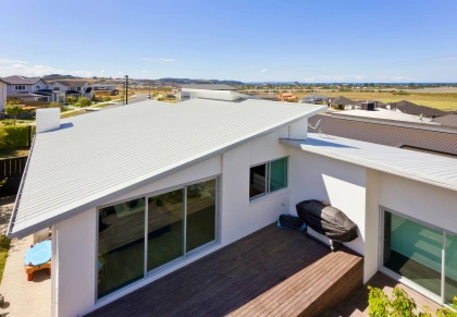 Modern house with sleek metal roofing and large glass windows overlooking a suburban neighborhood and open fields.