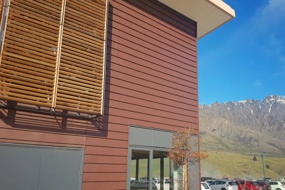 A modern commercial building featuring Weatherboards cladding in Corten Bronze, complemented by wooden shutters and a scenic mountain backdrop.