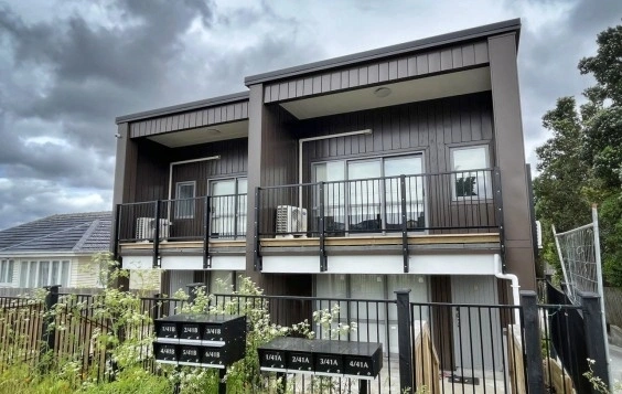 A modern residential building featuring Interlocking cladding in Ebony color, complemented by black railings and a landscaped foreground.