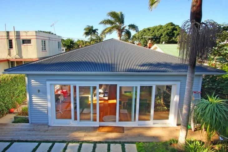 A small residential house featuring TRS Corrugate roofing in the Grey Friars colour, surrounded by lush greenery and a wooden deck.