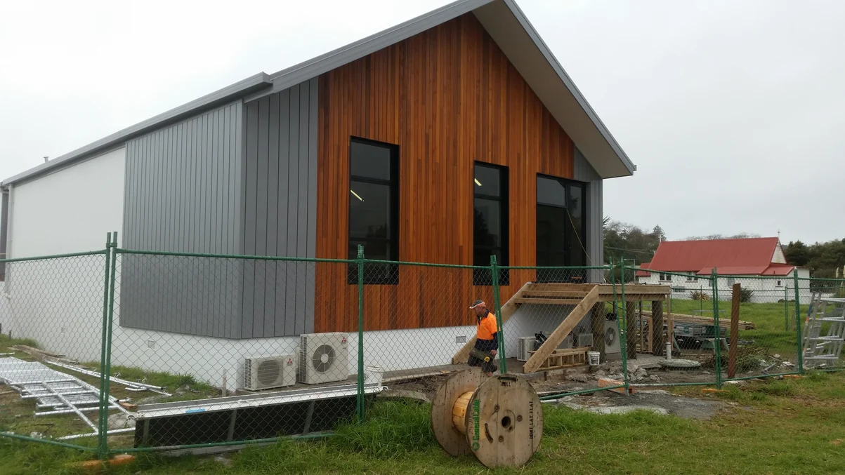 A two-story modern house with vertical dark grey steel cladding and natural wooden panels.