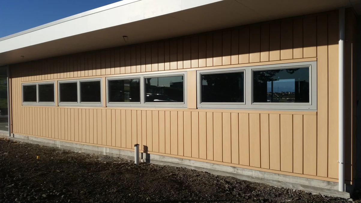 A long residential building with steel cladding in a natural wood finish and large windows overlooking a scenic landscape.