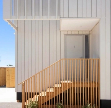 A modern architectural design featuring sleek white cladding and a wooden staircase leading to a minimalist entrance.