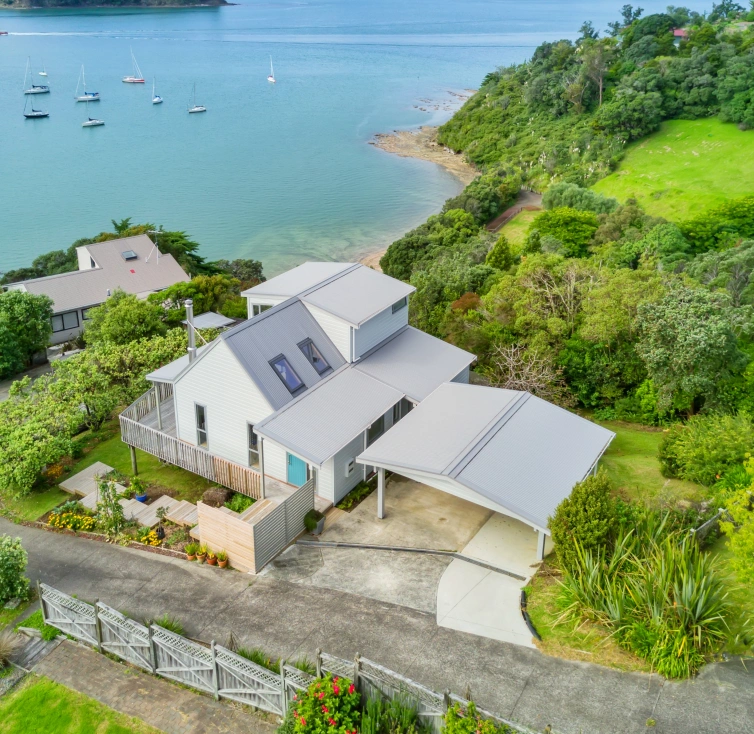 A beautiful residential property with a grey corrugated steel roof, overlooking a serene coastal view surrounded by lush greenery.