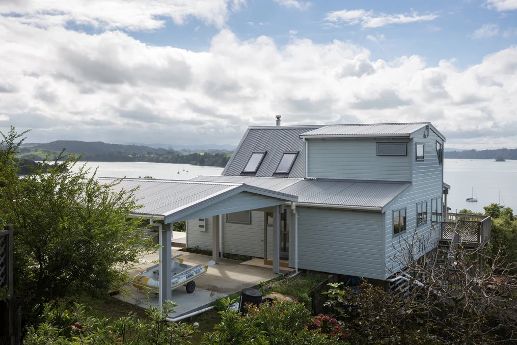 A coastal home with a grey corrugated metal roof, light blue cladding, and a stunning ocean backdrop.