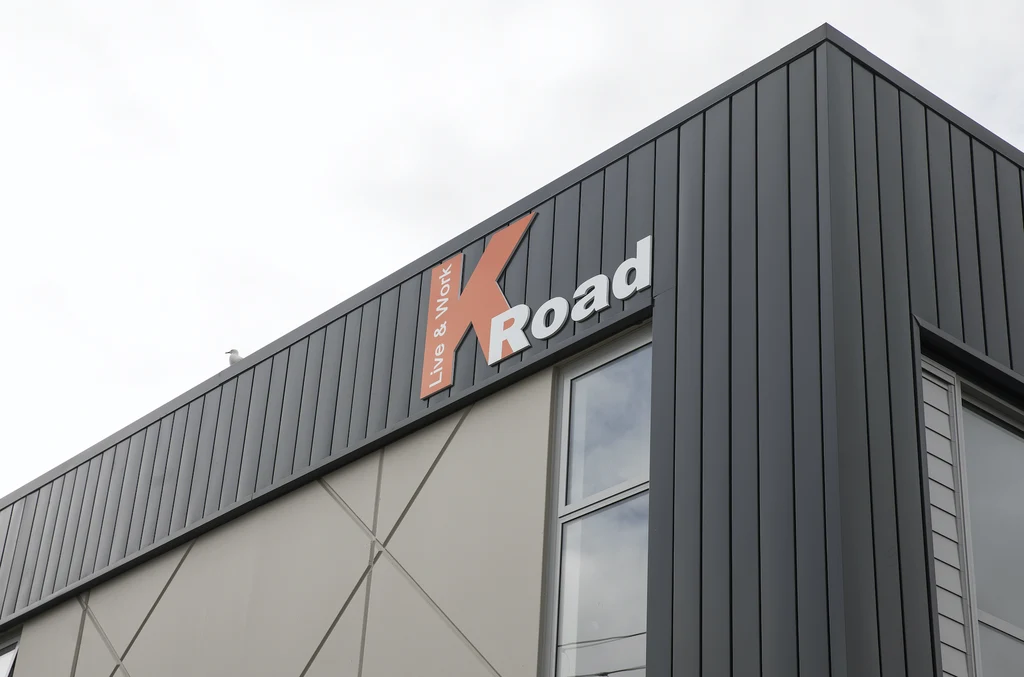 A commercial building with dark grey steel cladding and a prominent "K Road" sign on the façade.