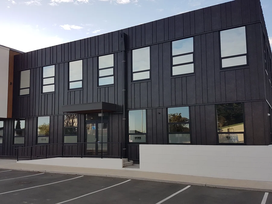 A commercial building with vertical black steel cladding and large square windows.