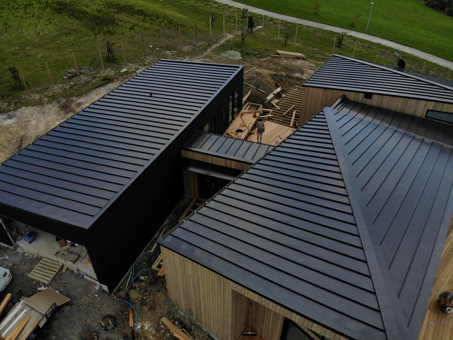 An aerial view of a contemporary home with interconnected structures and dark standing seam steel roofs.