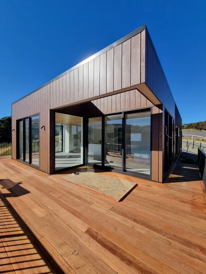 A modern single-storey home with timber decking and sleek vertical cladding under a clear blue sky.