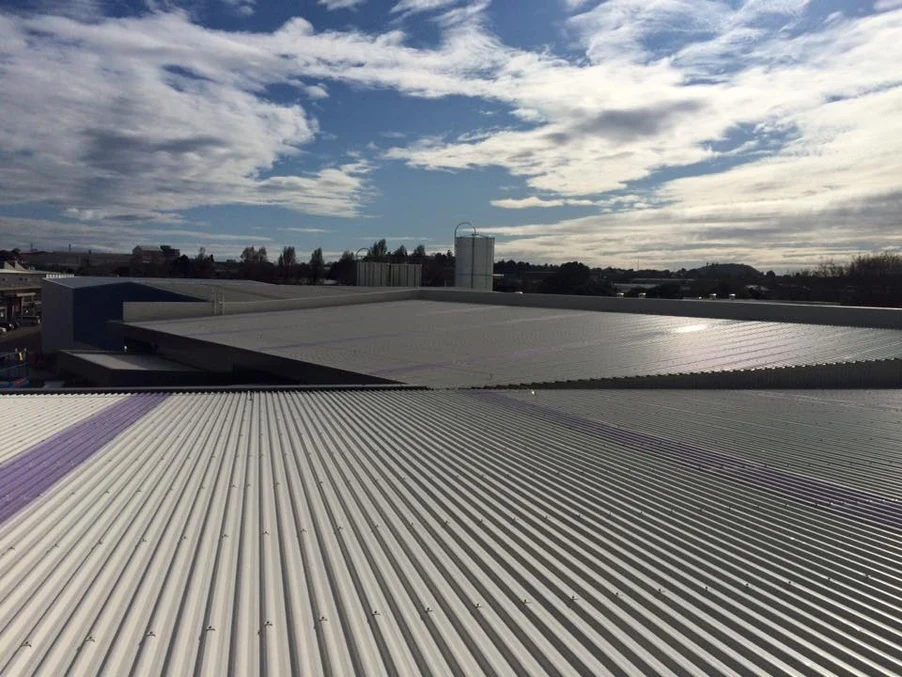 A wide industrial roof with white steel roofing panels under a bright sky.