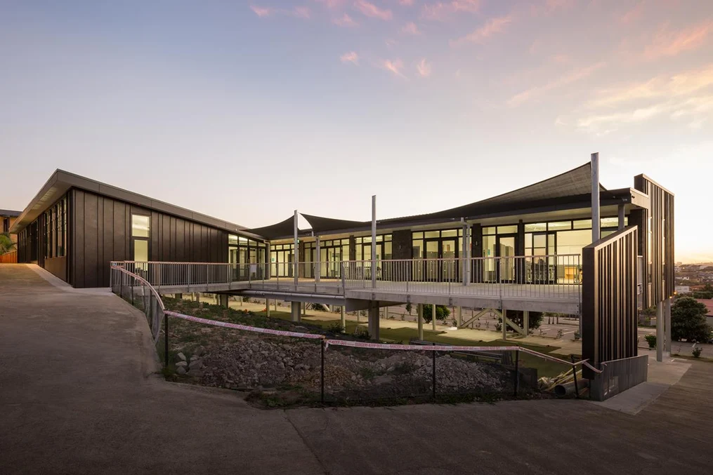 A modern educational or office building with black steel cladding and large windows at sunset.