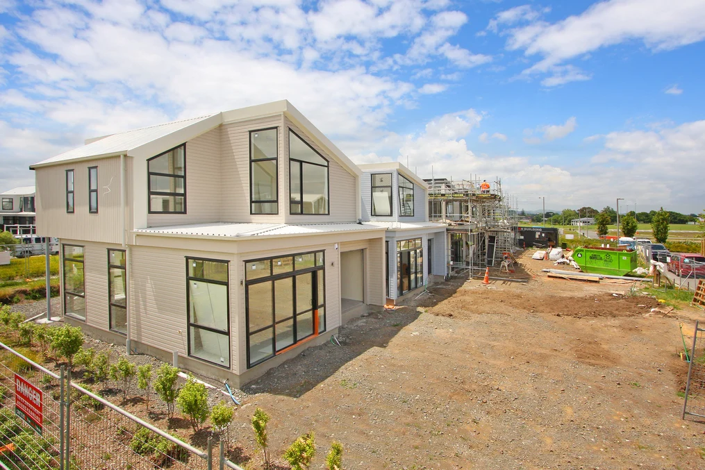 A large two-storey building under construction, featuring white cladding and grey metal roofing.