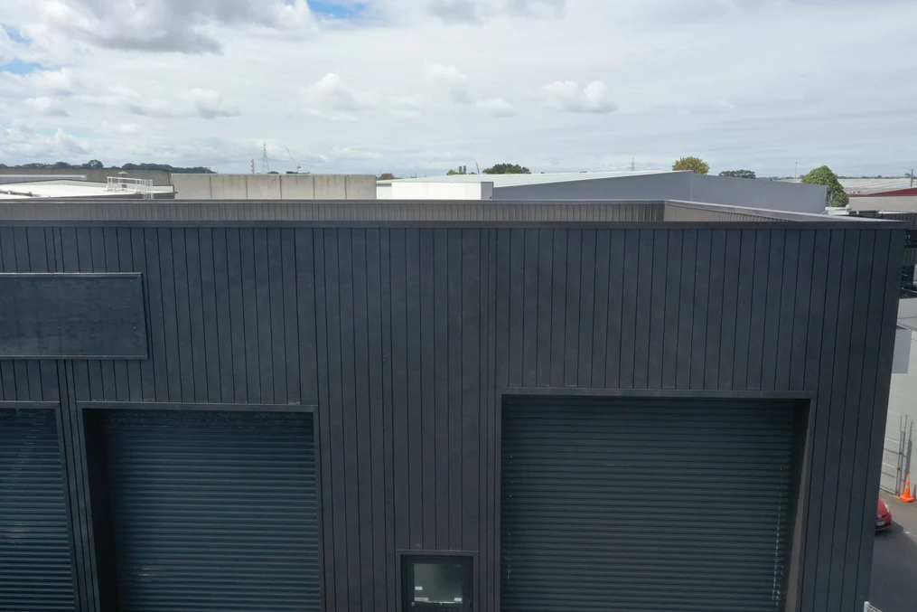 A commercial building with black vertical steel cladding and roller doors.