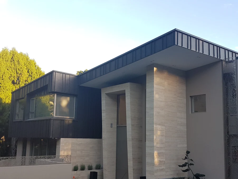 A modern residential home featuring a mix of black steel cladding and beige stone finishes.