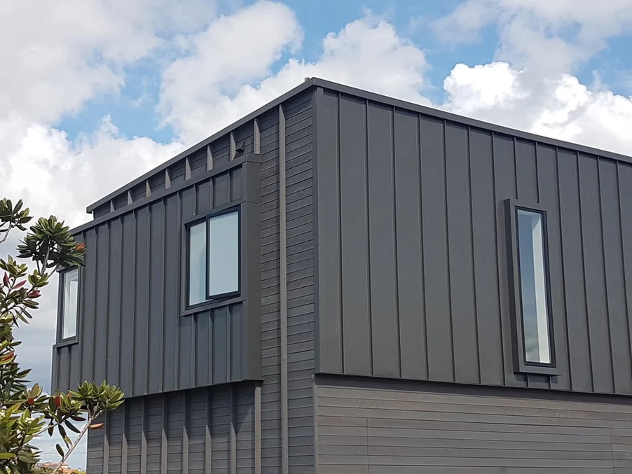 A modern residential building featuring vertical dark grey steel cladding and sleek, narrow windows.