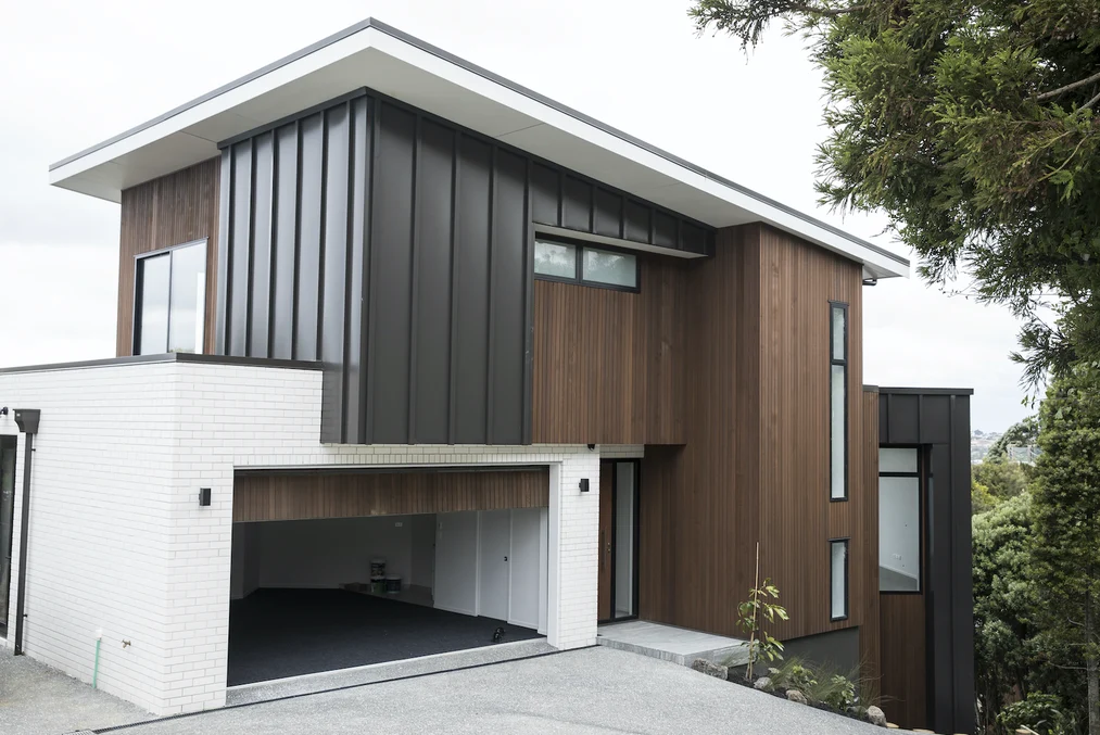 A single-story building with grey steel cladding and vertical wooden panels, under construction.