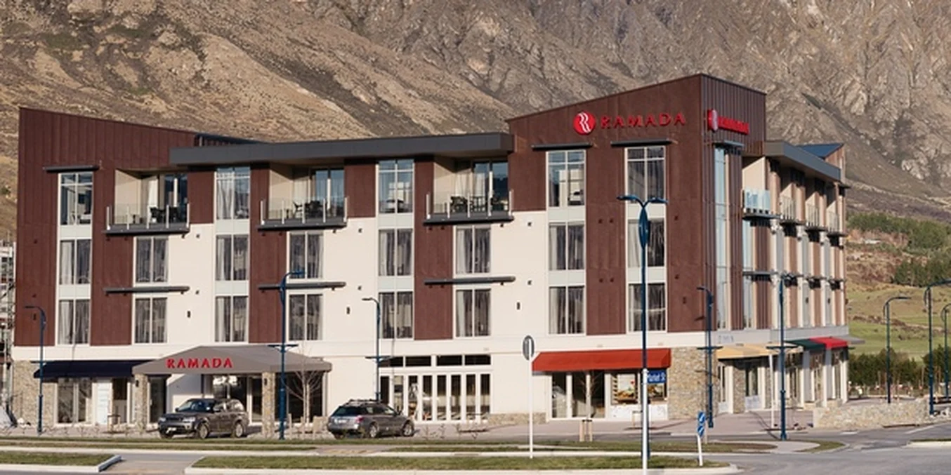 A hotel building set against a mountain backdrop, with dark steel cladding and natural finishes.