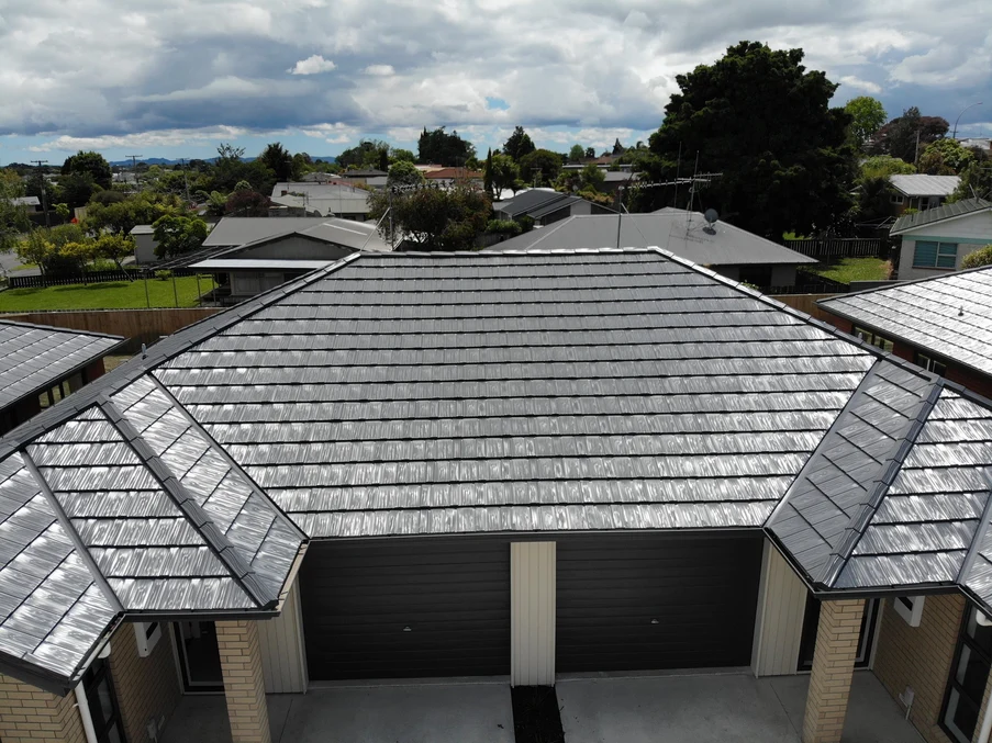 A close-up of a residential property with a tile-like metal roof in grey, surrounded by a suburban setting.