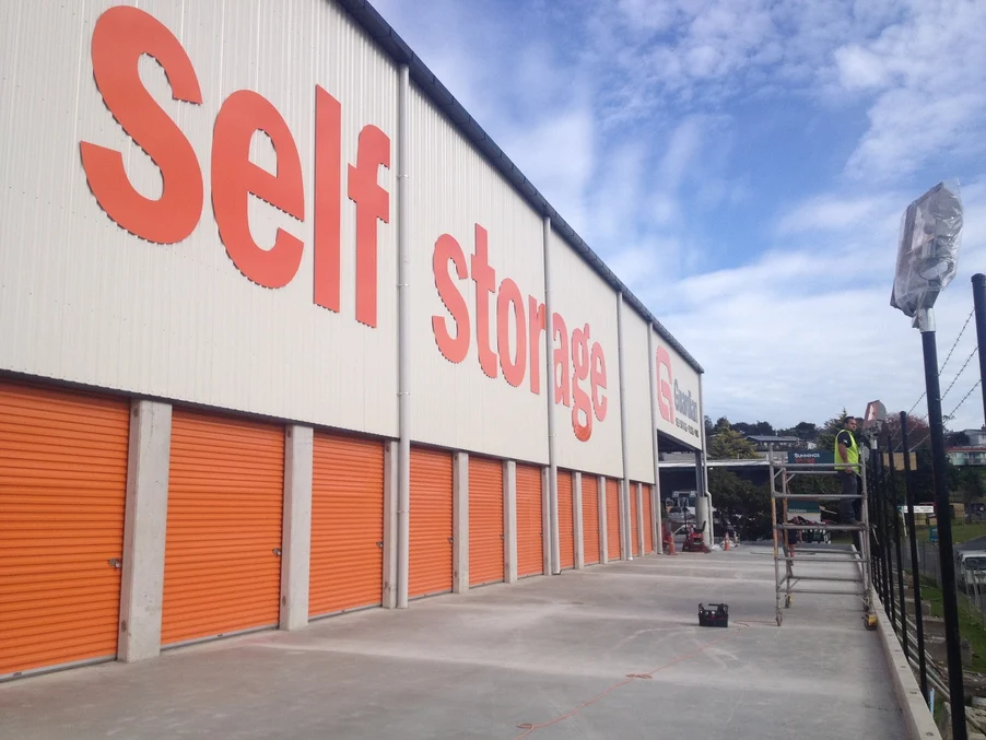 A large self-storage building with white steel cladding and bright orange roller doors.