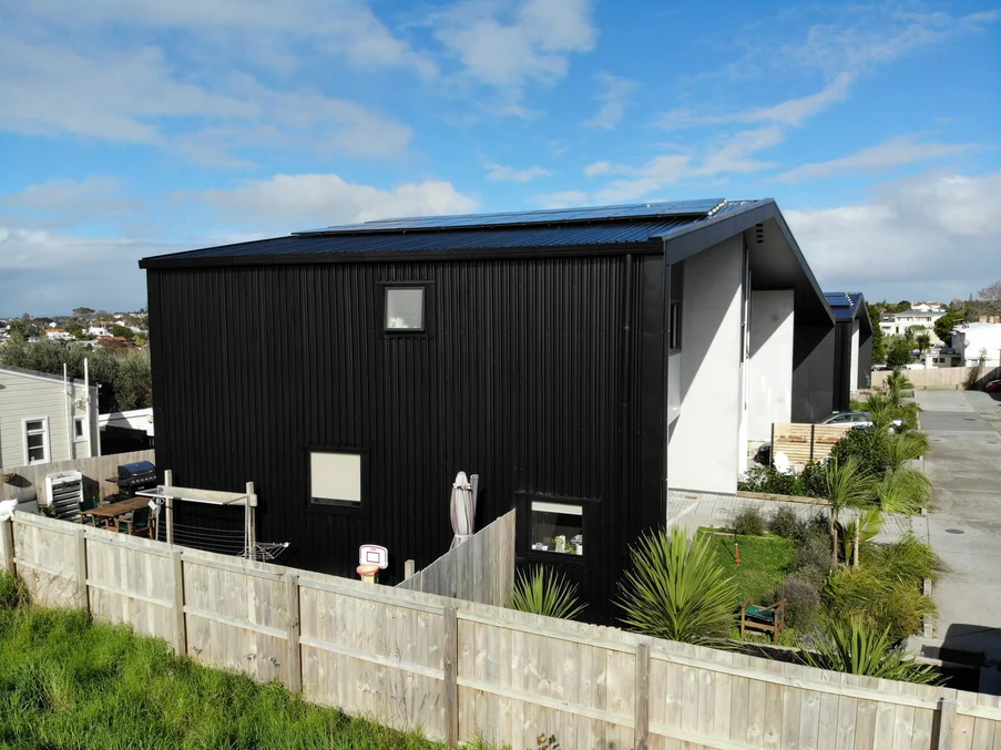 A contemporary black-clad townhouse with sleek metal roofing, surrounded by tropical greenery.