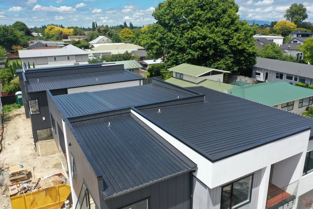 A row of modern homes with sleek black roofing and light-coloured cladding, situated in a suburban neighbourhood.